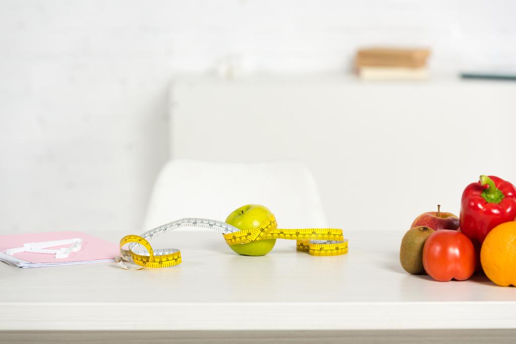 папка, измерительная лента и свежие фрукты и овощи на столе
 - Фото, изображение