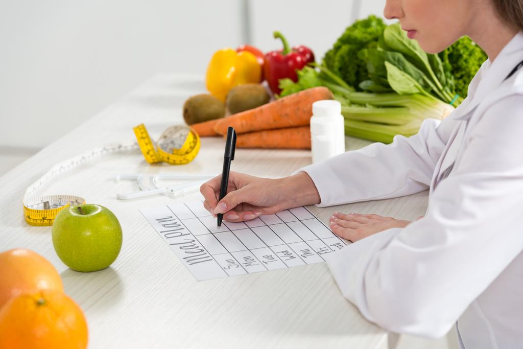 cropped view of dietitian writing in meal plan at workplace - Photo, Image