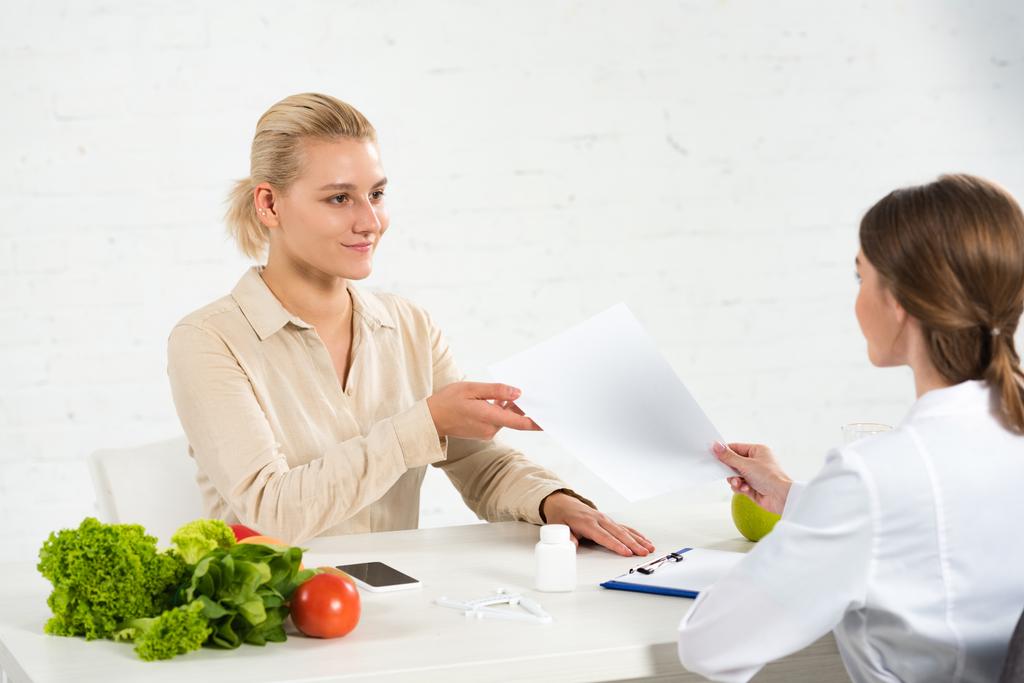 nutricionista em casaco branco dando papel ao paciente no local de trabalho
 - Foto, Imagem