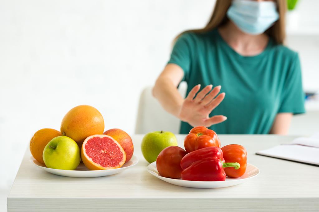 abgeschnittene Ansicht einer Frau in medizinischer Maske, die Obst und Gemüse zu Hause verweigert - Foto, Bild