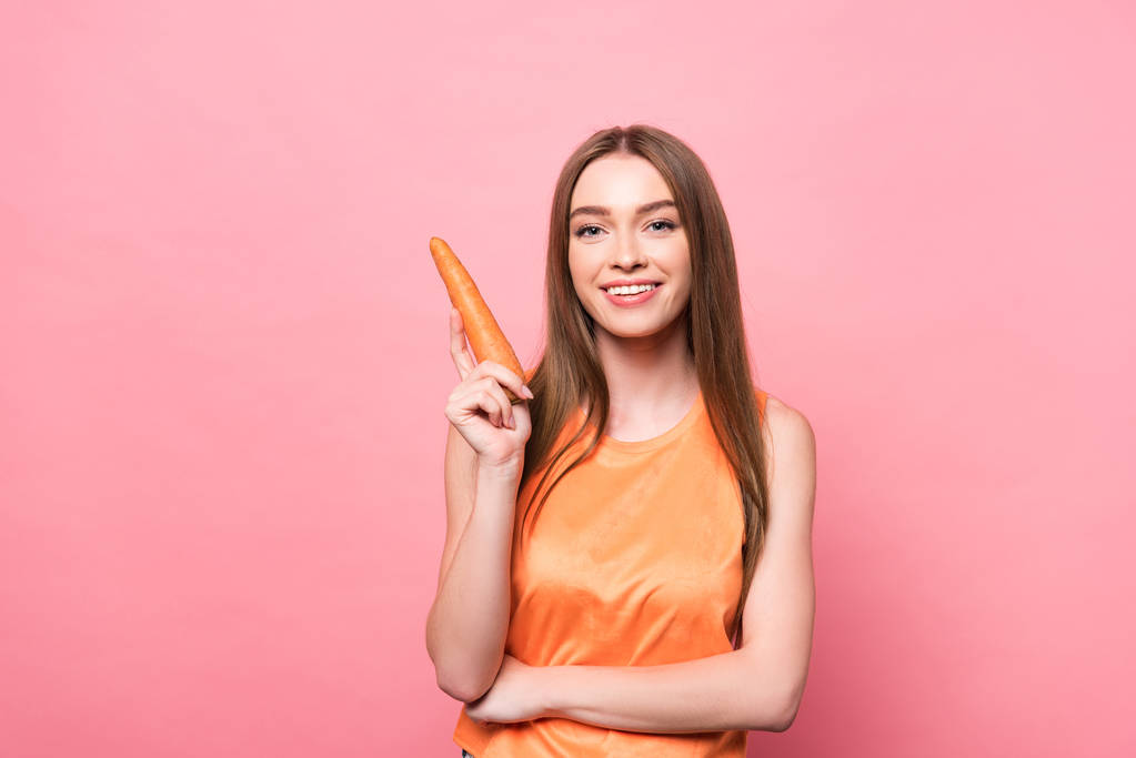 sorrindo atraente jovem segurando cenoura e olhando para a câmera em rosa
 - Foto, Imagem