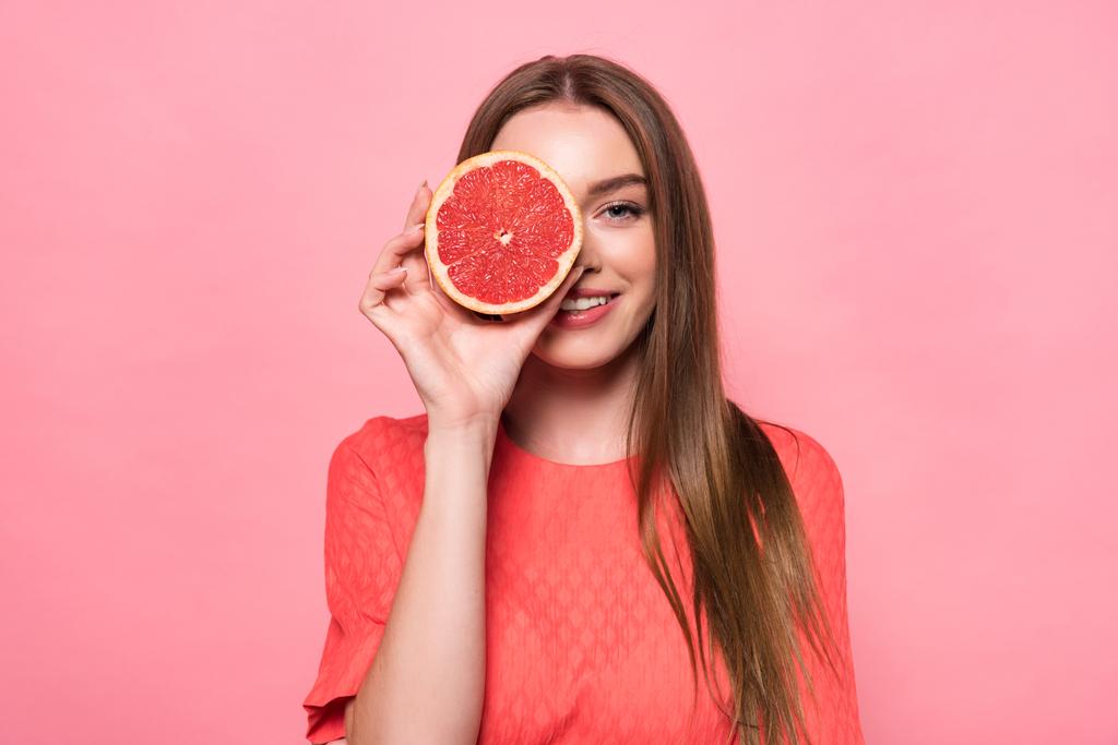 вид спереду приваблива усміхнена молода жінка тримає нарізаний грейпфрут ізольовано на рожевому
 - Фото, зображення