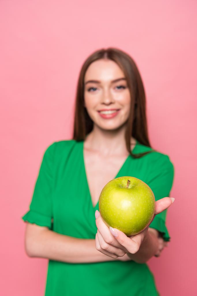 селективное внимание привлекательной молодой женщины, держащей зеленое яблоко и улыбающейся изолированно на розовом
 - Фото, изображение