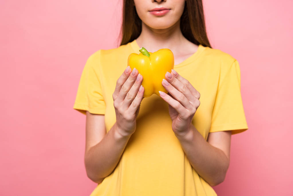 bijgesneden beeld van de jonge vrouw in t-shirt met gele paprika op roze - Foto, afbeelding