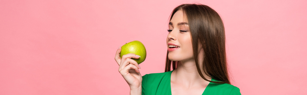 панорамный снимок привлекательной улыбающейся девушки с зеленым яблоком, изолированным на розовый
 - Фото, изображение