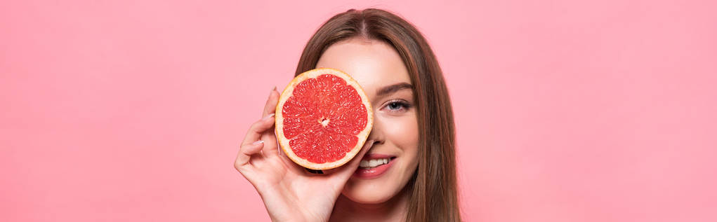 панорамный снимок улыбающейся привлекательной девушки с вырезанным грейпфрутом, изолированным на розовом
 - Фото, изображение