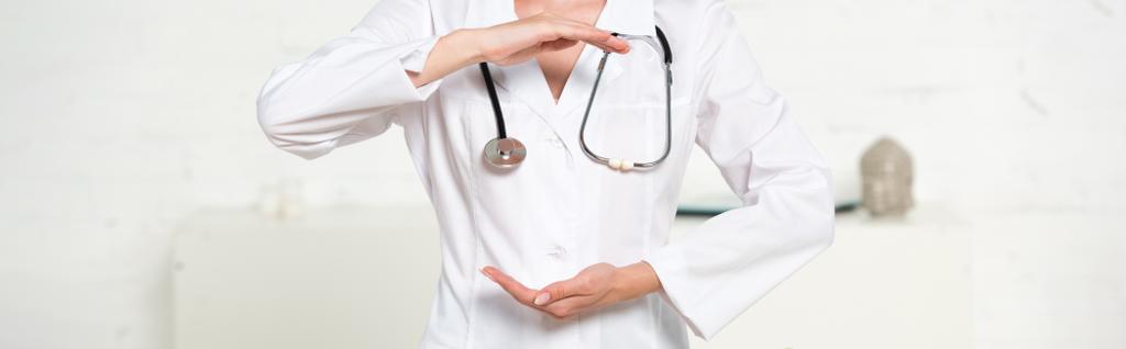 panoramiczny strzał lekarza w białym płaszczu z stetoskop wskazując w klinice - Zdjęcie, obraz