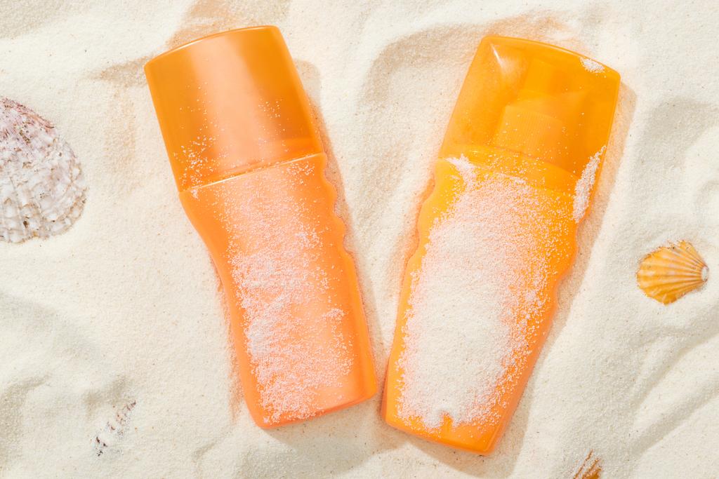Orangefarbene Flaschen Sonnencreme auf Sand mit Muscheln - Foto, Bild