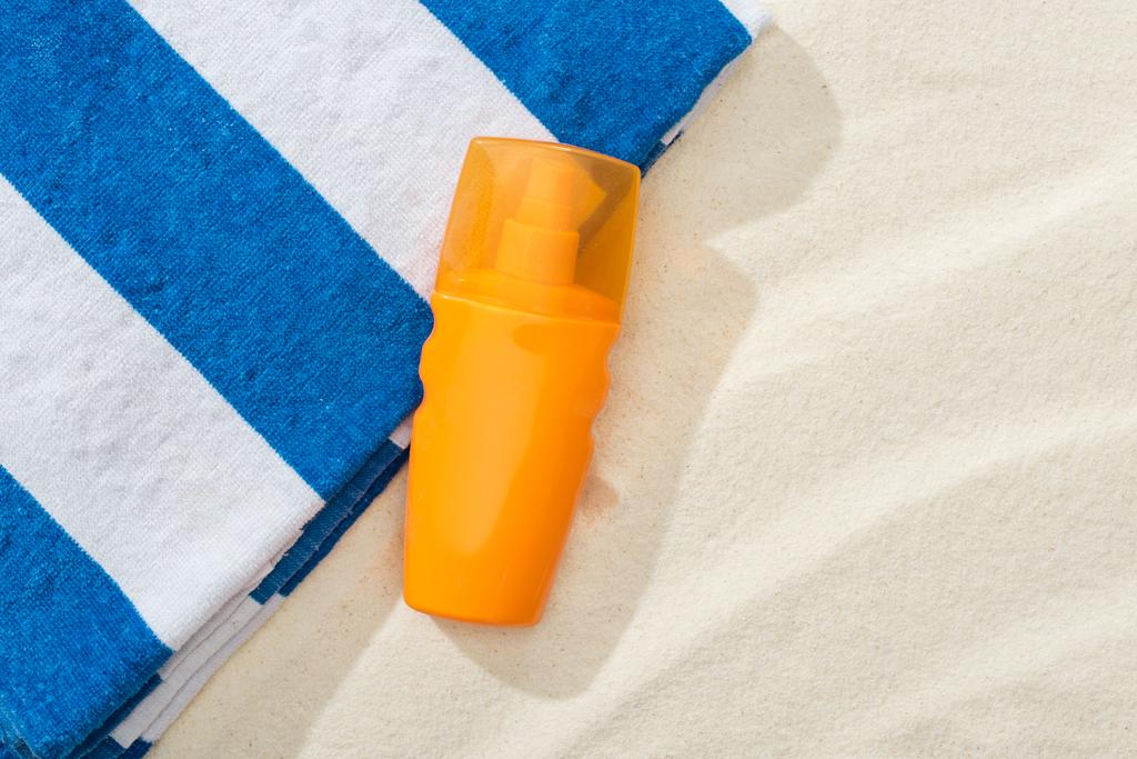 ストライプタオルで砂の上に日焼け止めのオレンジ色のボトル - 写真・画像