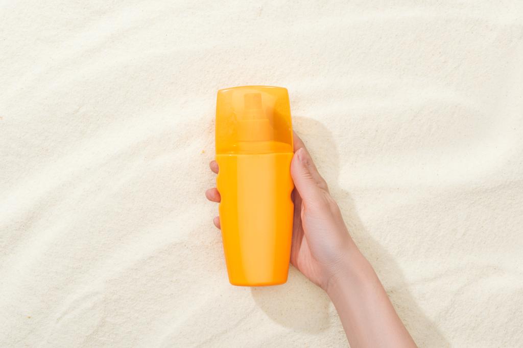 vista ritagliata della donna con crema solare arancione sopra la sabbia dorata
 - Foto, immagini