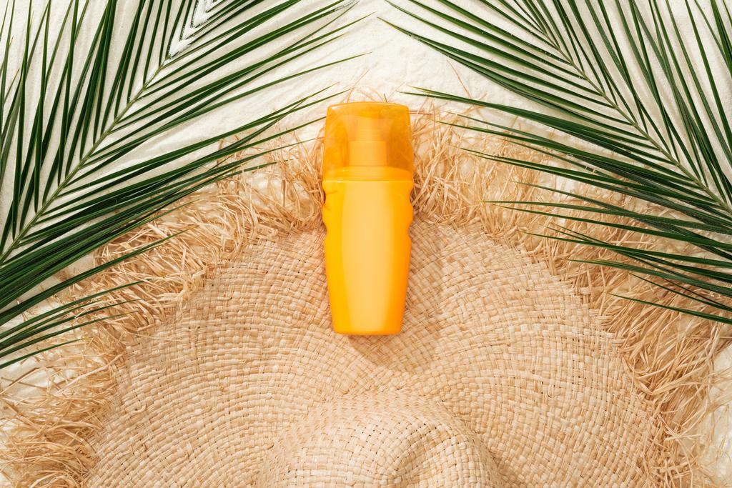 Widok z góry na stylowy kapelusz słomkowy na złotym piasku z zielonymi liści palmowych i filtrem przeciwsłonecznym - Zdjęcie, obraz