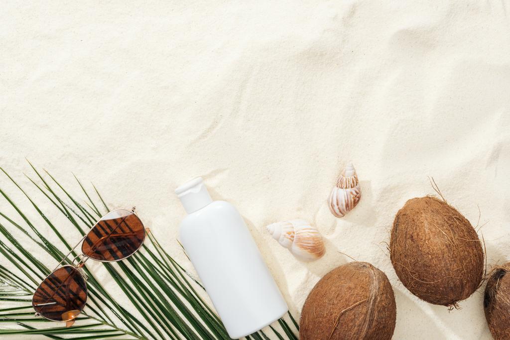 top view of seashells, coconuts and sunscreen lotion, sunglasses and palm leaf on sand - Photo, Image