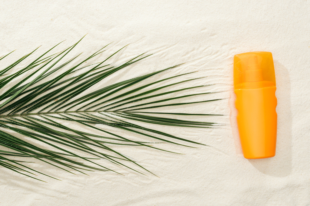 ylhäältä näkymä palmunlehtiä ja oranssi aurinkovoidetta spray hiekalla
  - Valokuva, kuva