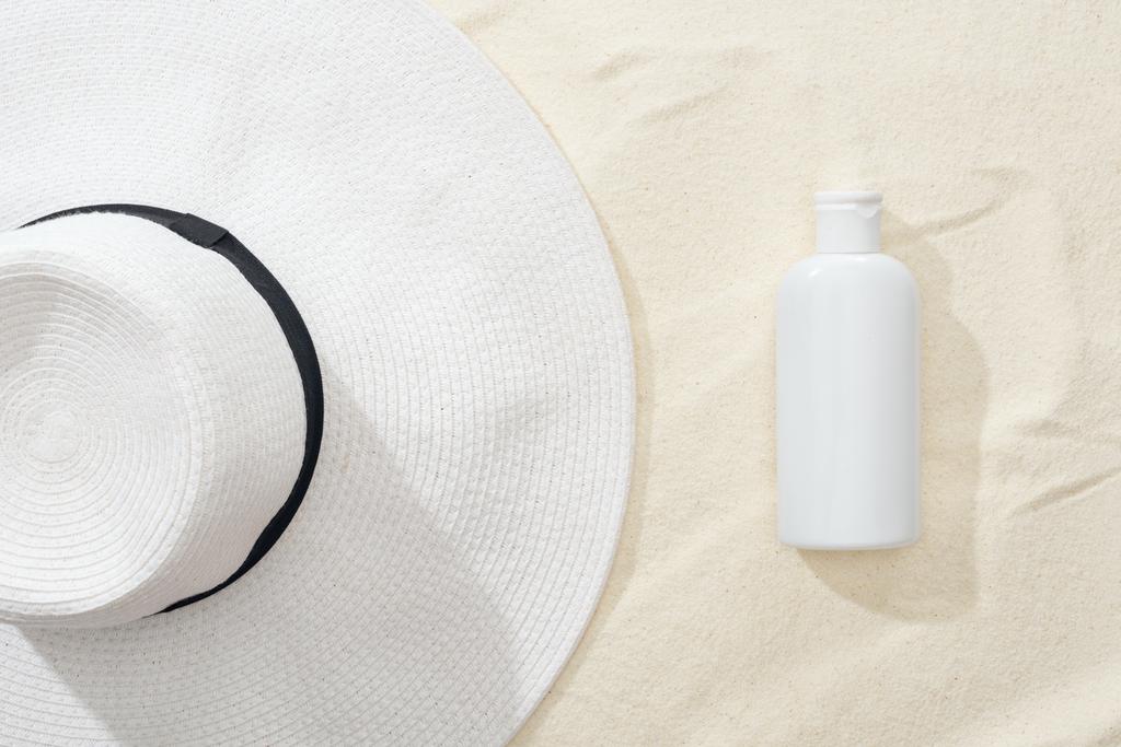 top view of white sunscreen lotion and straw hat on sand - Photo, Image