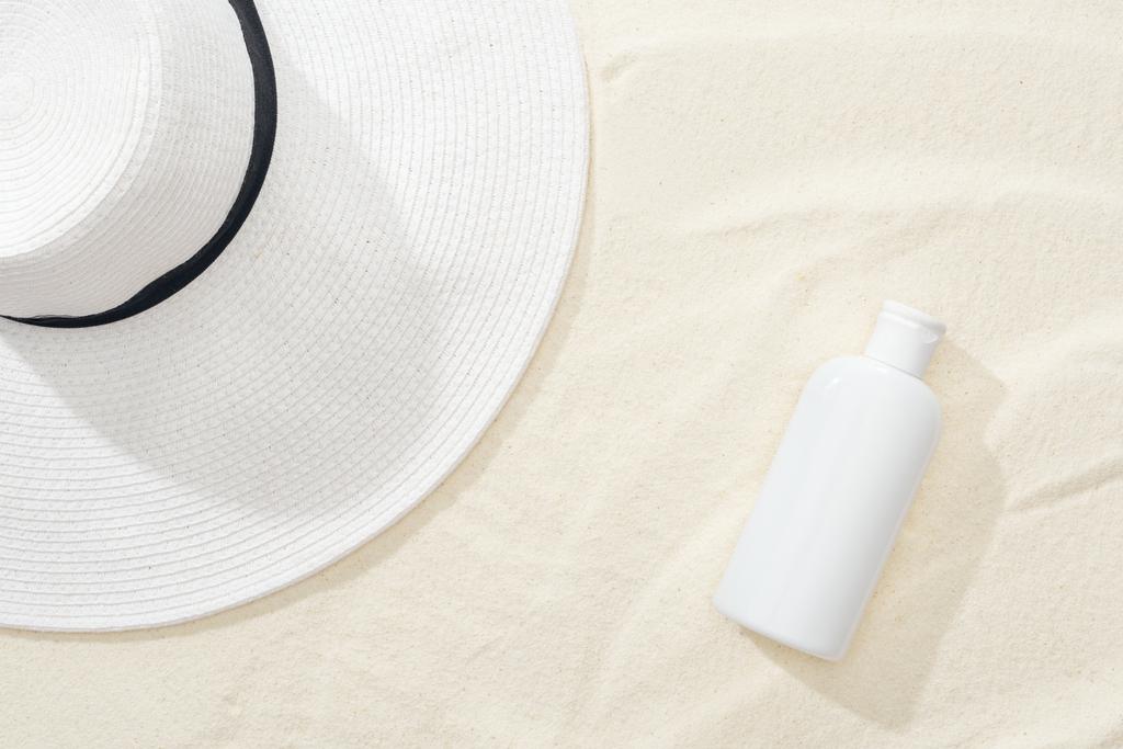 Widok z góry biały krem do opalania i słomkowy kapelusz na piasku - Zdjęcie, obraz