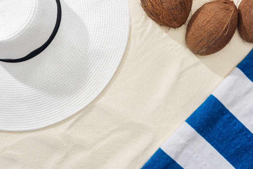 vista superior de cocos, toalla rayada y sombrero de paja blanco sobre arena
 - Foto, imagen