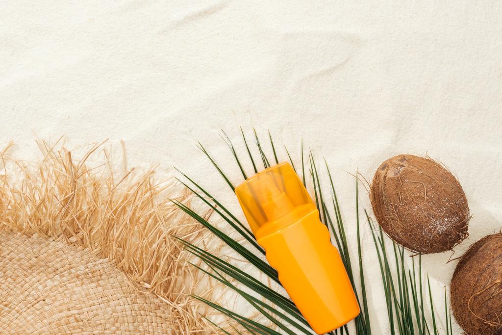 вид сверху пальмового листа, оранжевый солнцезащитный крем, кокосы и соломенная шляпа на песке
 - Фото, изображение