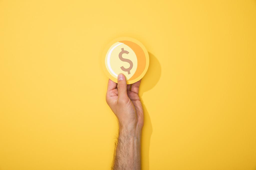 обрезанный вид человека с бумажной иконой золотой монеты на желтом фоне
 - Фото, изображение
