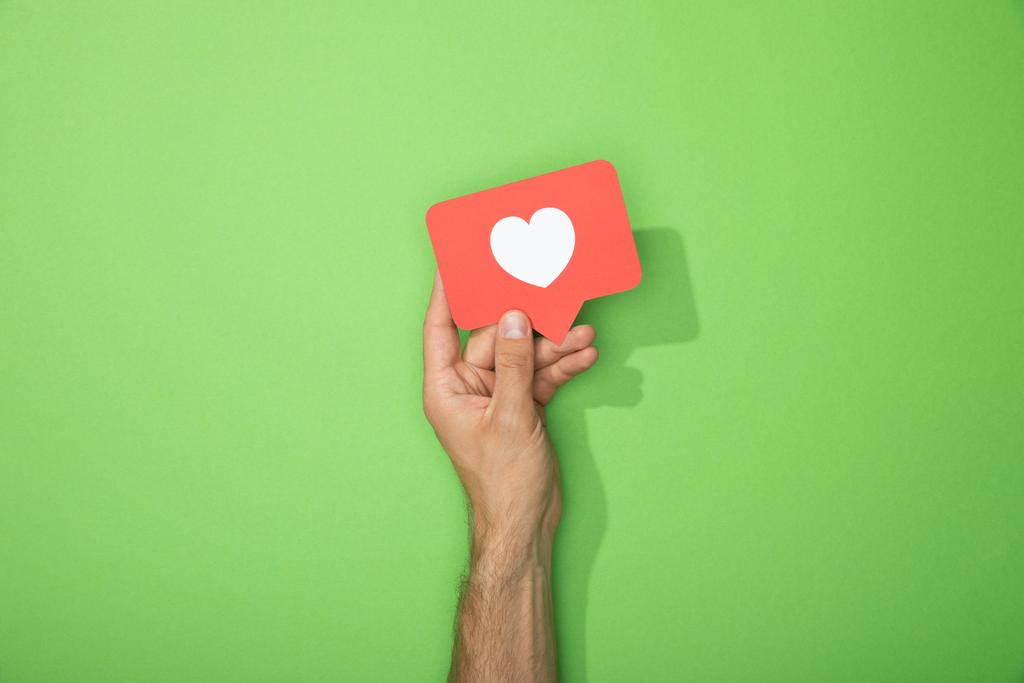 vista recortada del hombre sosteniendo icono de papel rojo con corazón blanco en verde
 - Foto, Imagen