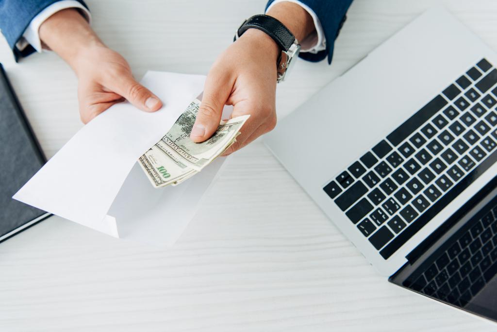 masada laptop yakın dolar banknotlar ile işadamı tutan zarf üst görünümü  - Fotoğraf, Görsel