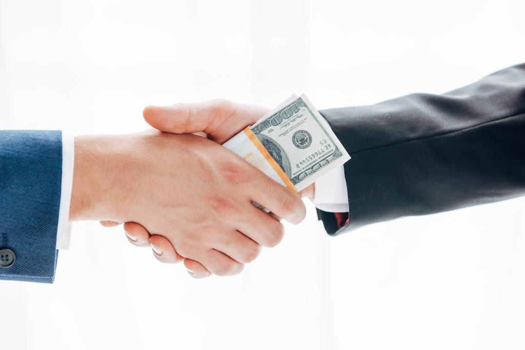 bijgesneden beeld van de man geven omkopen aan zakenpartner terwijl schudden handen geïsoleerd op wit - Foto, afbeelding