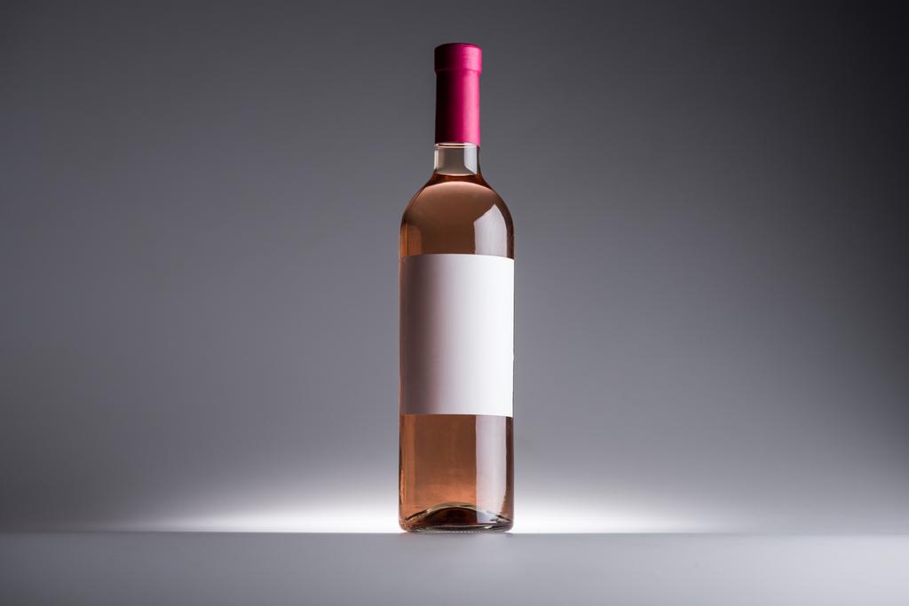 пляшка трояндового вина і порожня етикетка на темному фоні з заднім світлом
 - Фото, зображення