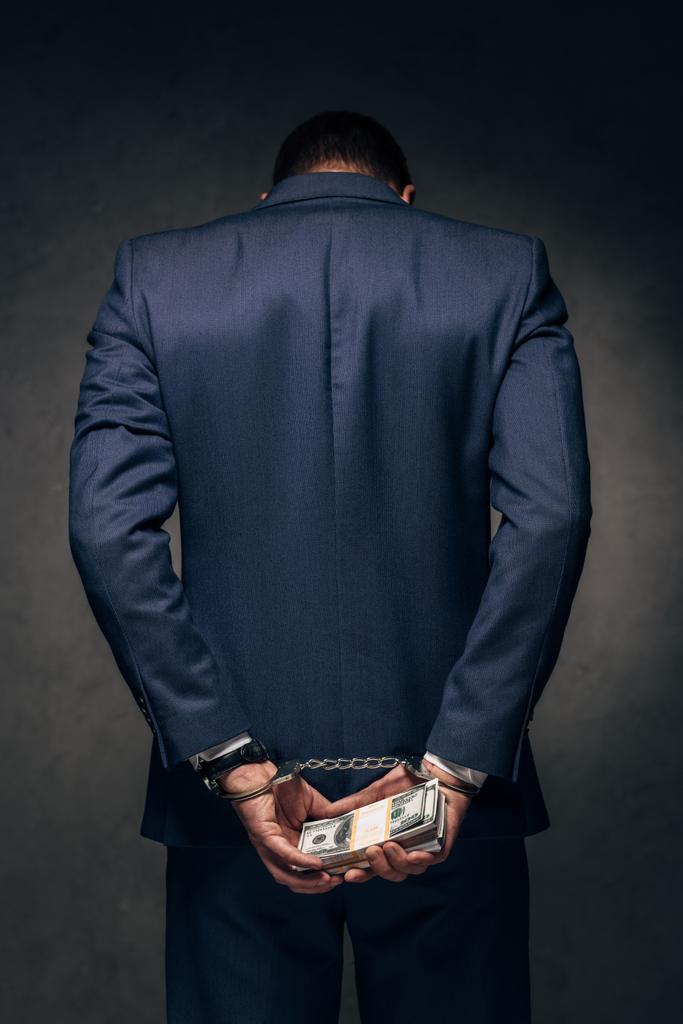 вид сзади человека в наручниках в костюме, держащего взятку на сером
  - Фото, изображение