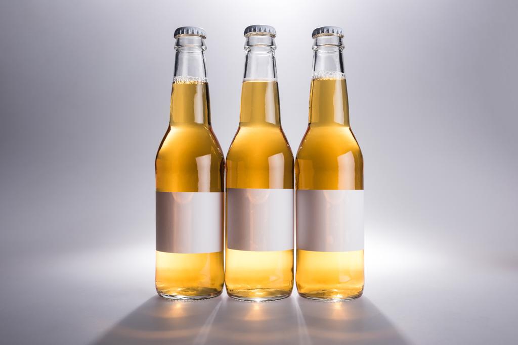 three glass bottles with beer with white labels on grey background - Photo, Image