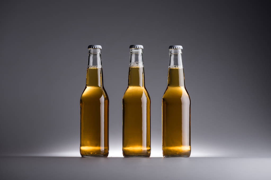 три стеклянные бутылки с пивом подряд на сером фоне
 - Фото, изображение