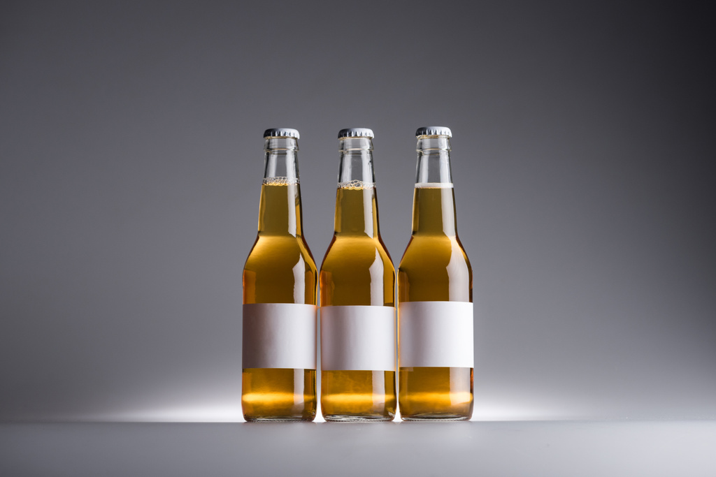 tres botellas de vidrio con cerveza y etiquetas blancas en fila sobre fondo oscuro
  - Foto, imagen