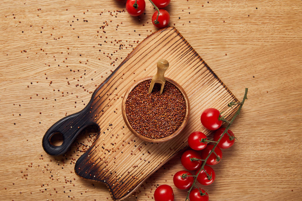 верхний вид семян красного киноа в деревянной чаше на доске для рубки рядом с красными помидорами
 - Фото, изображение