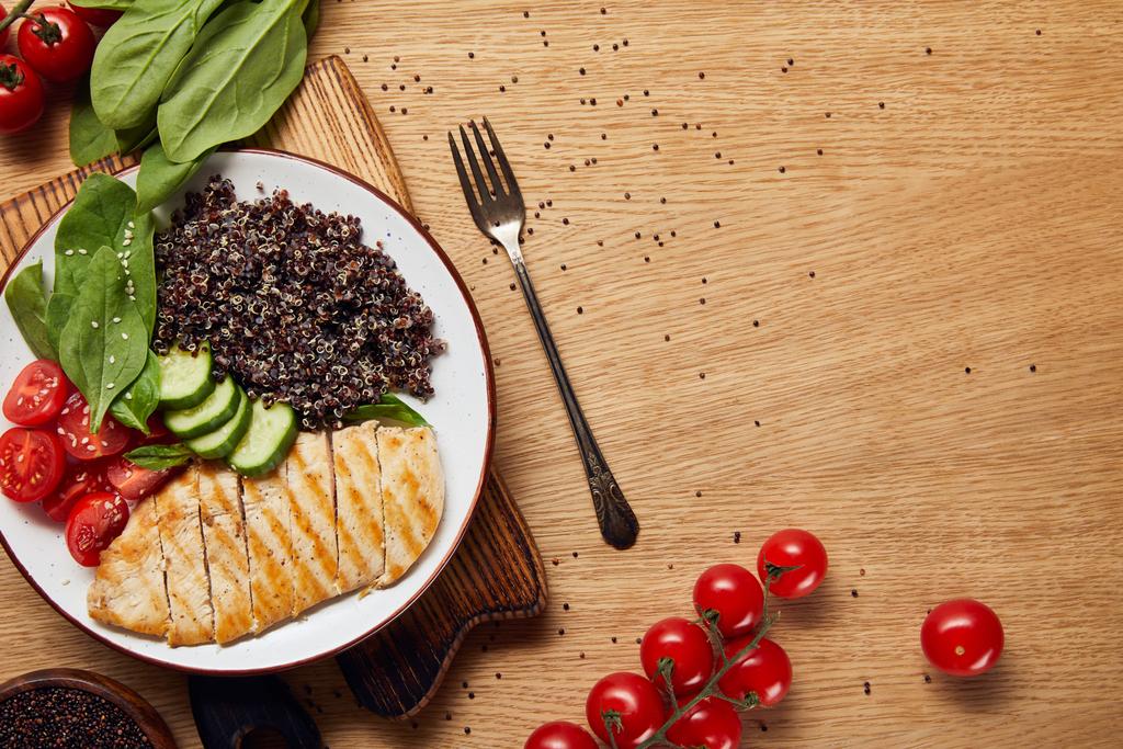 çatal ile ahşap masa üzerinde beyaz tabak üzerinde ızgara tavuk göğsü ve sebze ile pişmiş Quinoa üst görünümü - Fotoğraf, Görsel
