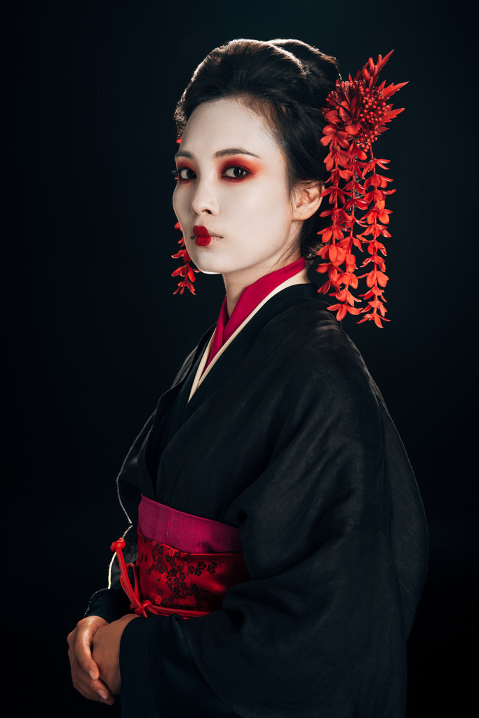 Geisha in zwarte en rode kimono en bloemen in haar geïsoleerd op zwart - Foto, afbeelding