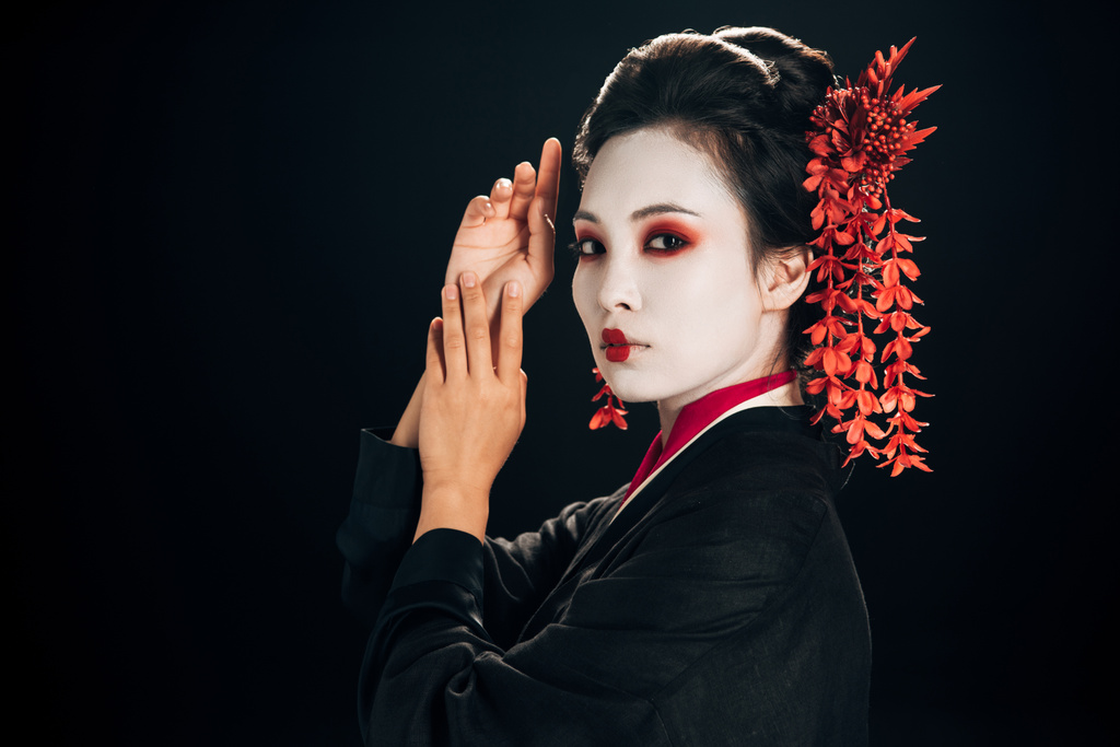 pohled na krásnou geishu v černém a červeném kimonu a květiny ve vlasech izolované na černém - Fotografie, Obrázek