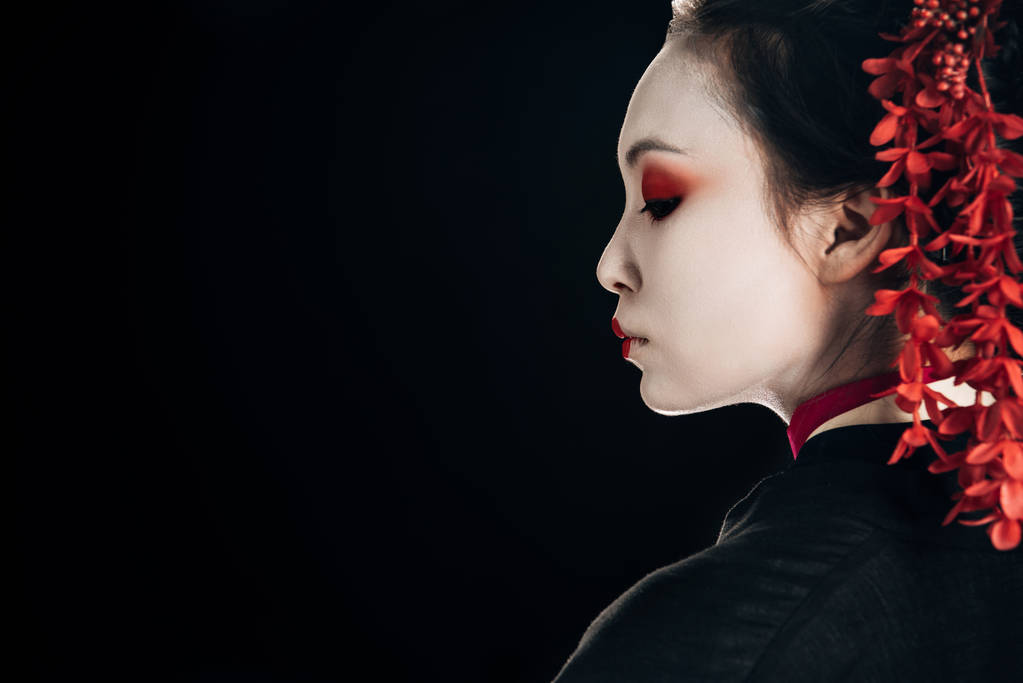 Profil der schönen Geisha in schwarzem und rotem Kimono und Blumen im Haar isoliert auf schwarz mit Kopierraum - Foto, Bild