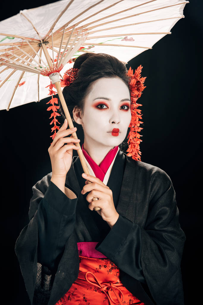 piękna gejsza w kimono z czerwonymi kwiatami we włosach posiadających tradycyjny azjatycki parasol na białym tle - Zdjęcie, obraz
