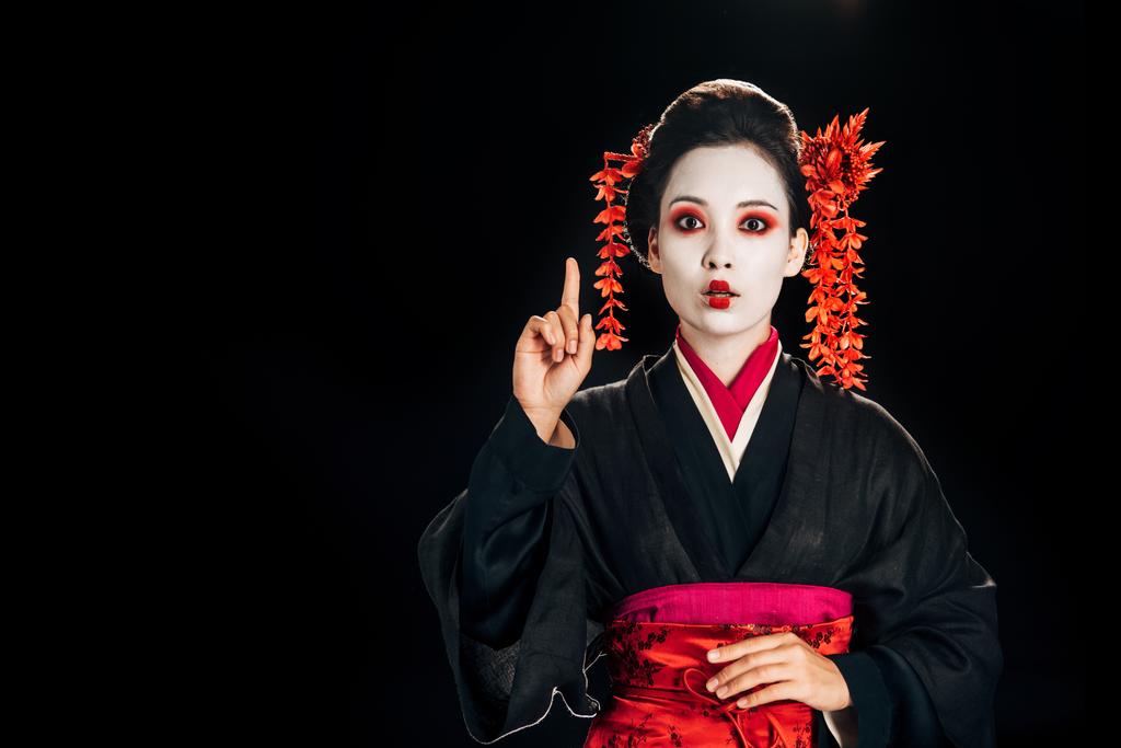 megdöbbentett gyönyörű gésa fekete és piros kimonó és virágok haját bemutató ötlet gesztus elszigetelt a fekete másolási tér - Fotó, kép