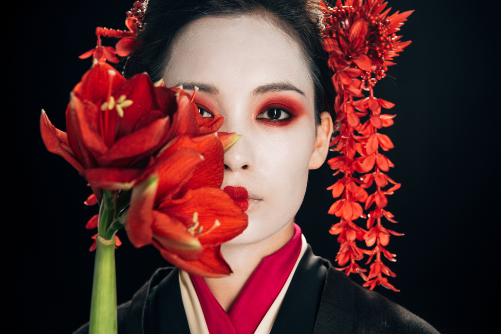 Porträt der schönen Geisha im schwarzen Kimono mit roten Blüten isoliert auf schwarz - Foto, Bild