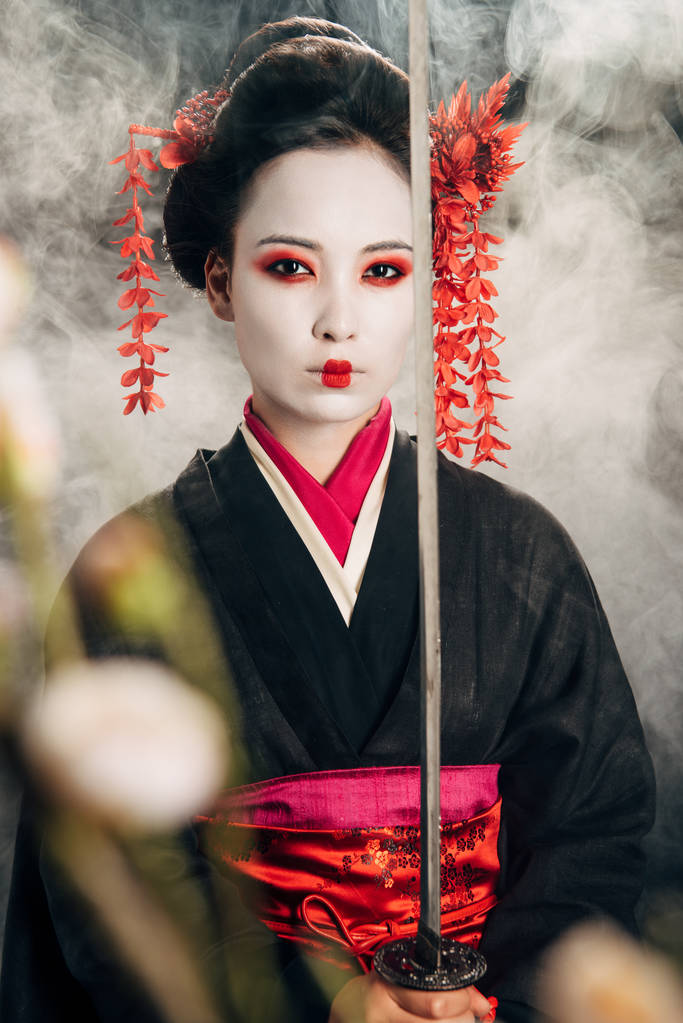 foyer sélectif de belle geisha en kimono noir tenant katana en fumée et branches de sakura
 - Photo, image