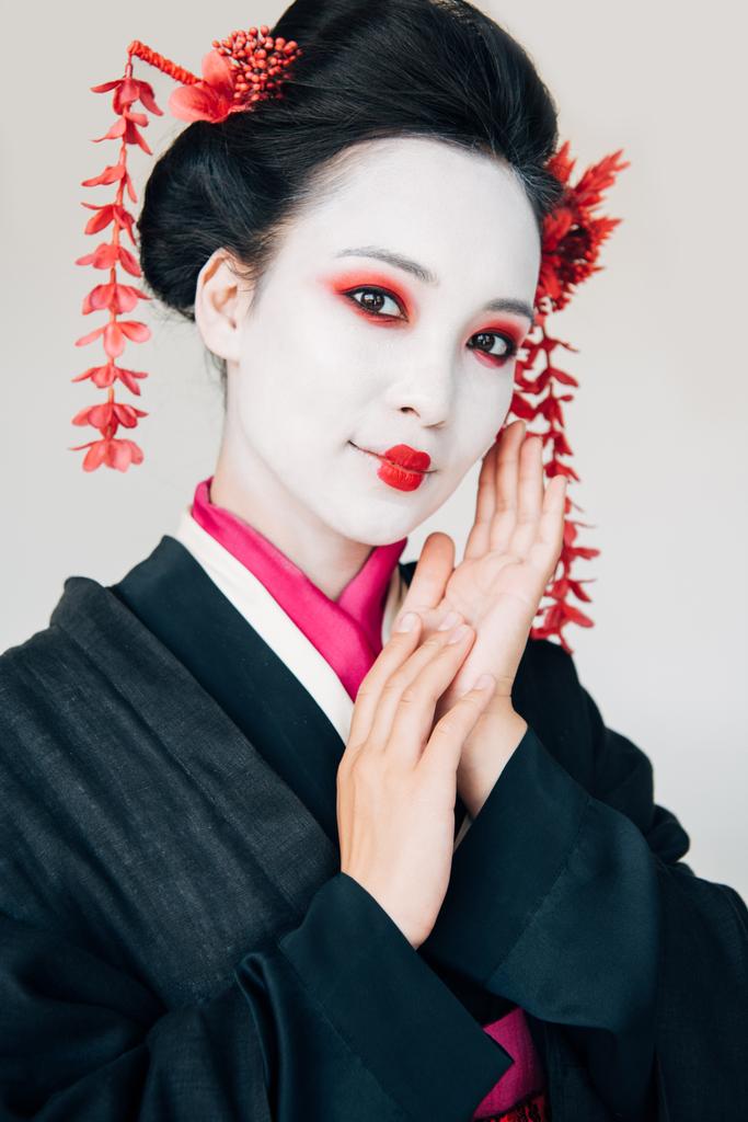 cheerful beautiful geisha in black kimono with red flowers in hair isolated on white - Photo, Image