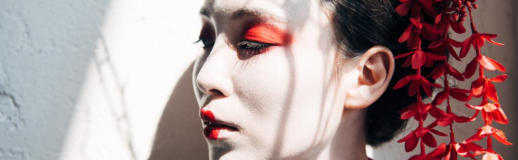 retrato de hermosa geisha con maquillaje rojo y blanco a la luz del sol con sombras, plano panorámico
 - Foto, Imagen