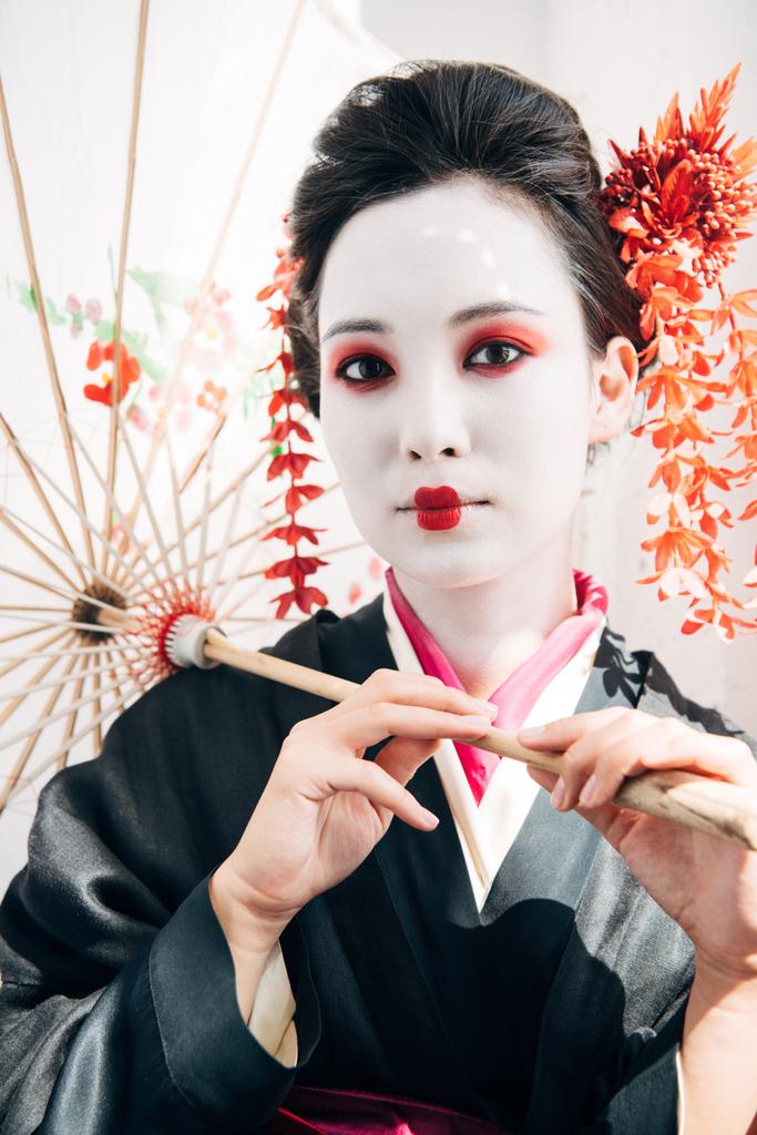 Schöne Geisha mit rot-weißem Make-up und Regenschirm in der Sonne - Foto, Bild