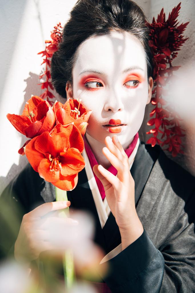 selektivní zaměření sakurských větví a krásné gejša s červenými květy na slunci - Fotografie, Obrázek