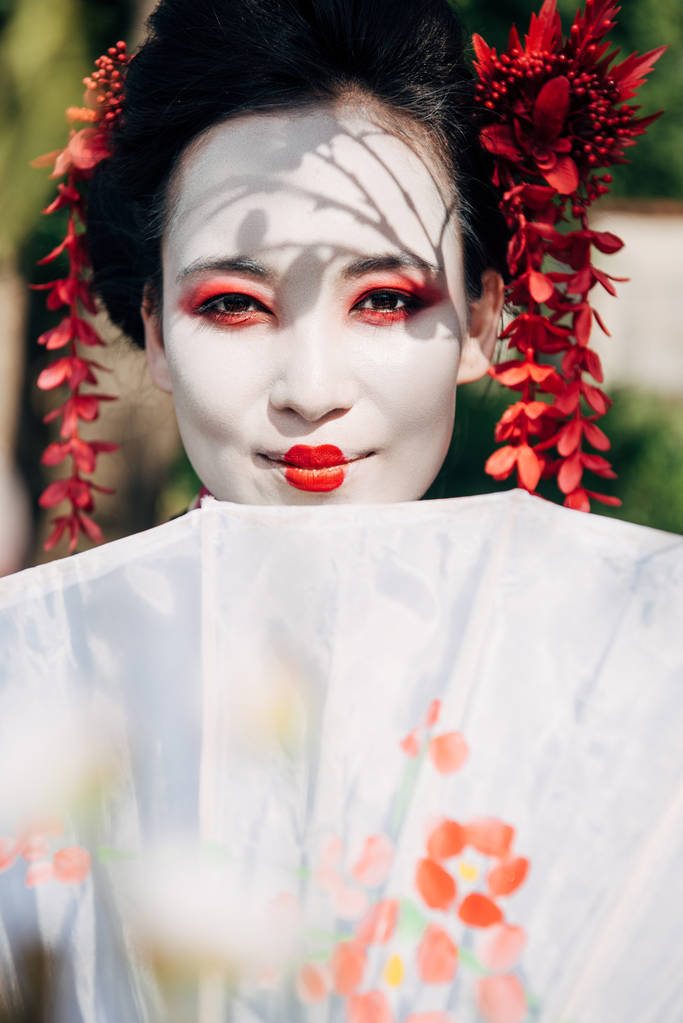 enfoque selectivo de ramas de árboles y hermosas geishas sonrientes con paraguas a la luz del sol
 - Foto, imagen