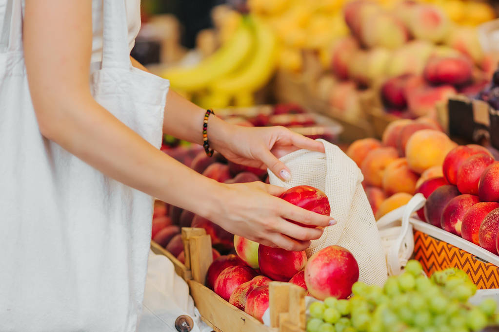 As mãos femininas colocam frutas e legumes no saco de produtos de algodão no mercado de alimentos. Saco ecológico reutilizável para compras. Conceito de resíduo zero
. - Foto, Imagem