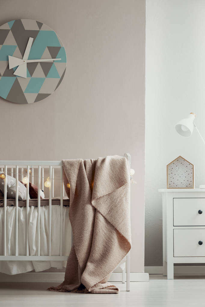 Elegante clack en la pared del elegante interior del dormitorio de bebé con cuna de madera blanca con manta rosa pastel y luces de bolas de algodón
 - Foto, imagen