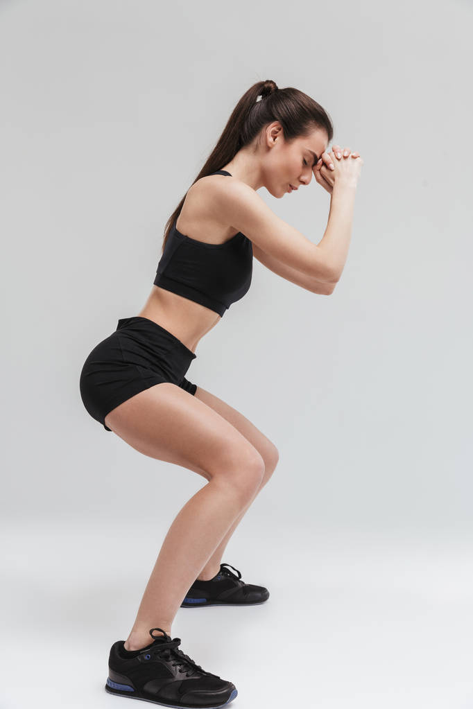 Όμορφη νεαρή Sport Fitness γυναίκα κάνει ασκήσεις απομονώνονται πάνω από γκρι τοίχο φόντο. - Φωτογραφία, εικόνα