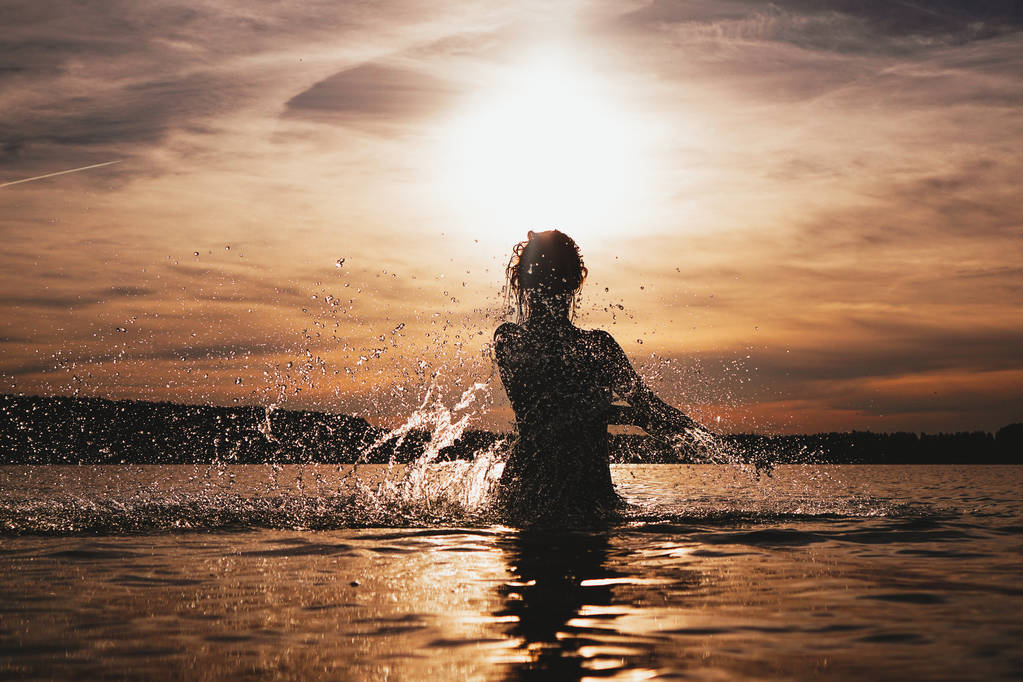 Jeune mannequin nageant dans la mer - coucher de soleil. Silhouette attrayante avec spray
 - Photo, image
