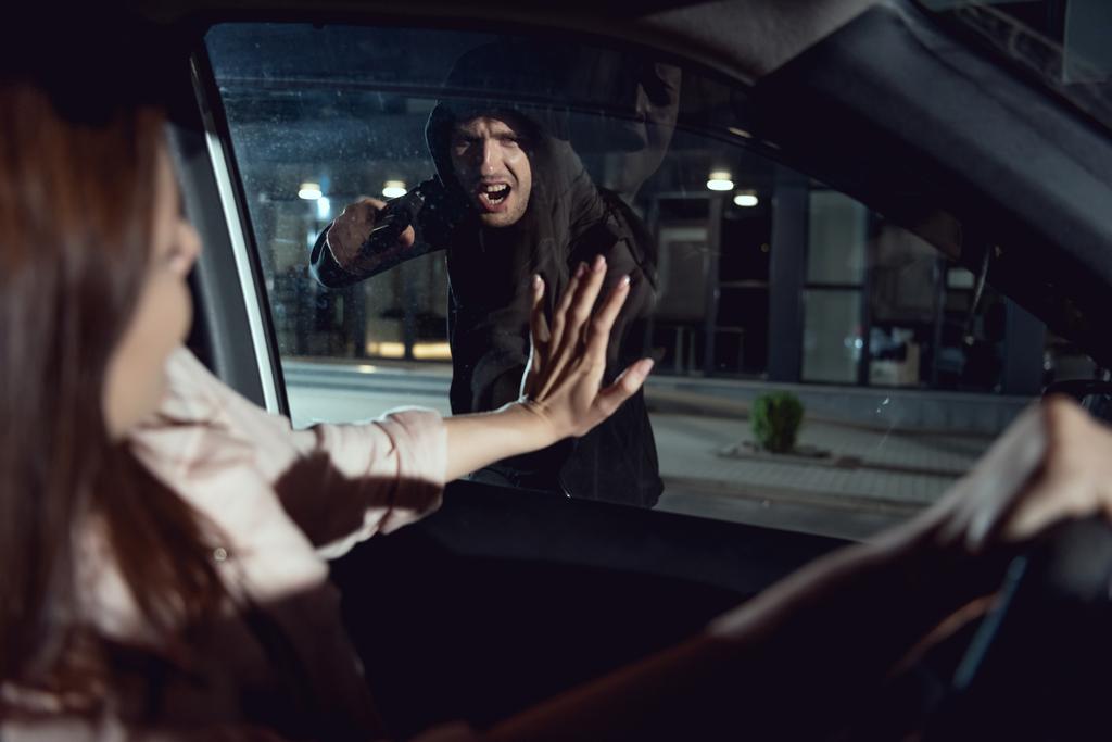 сердитий злодій вказує пістолет на жінку, сидячи в машині вночі
 - Фото, зображення