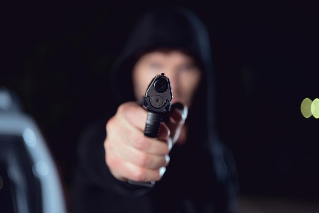 selektivní zaměření zbraně v rukou zloděje v černém plášti  - Fotografie, Obrázek